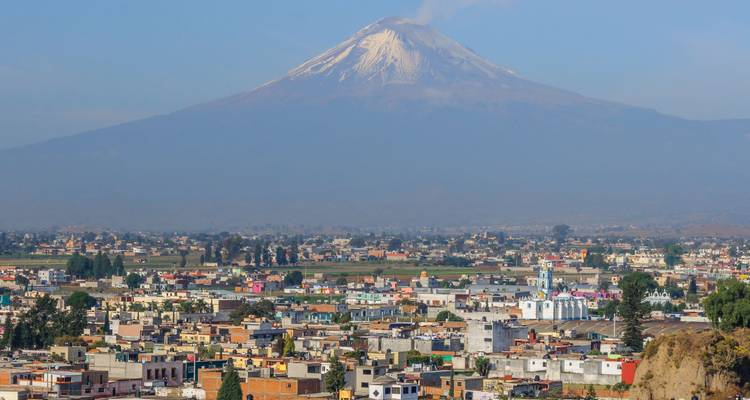Snow-capped Popocatépetl volcano towers above the cityscape of Puebla in the hazy morning light.