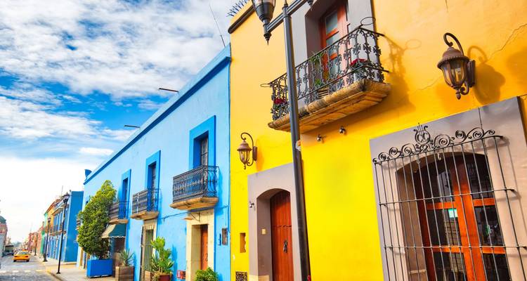 Brightly painted colonial houses with wrought-iron balconies lining a sunny street in Oaxaca.