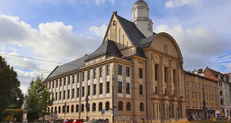 Stately beige-stone town hall style building with clock tower set against a partly cloudy blue sky.