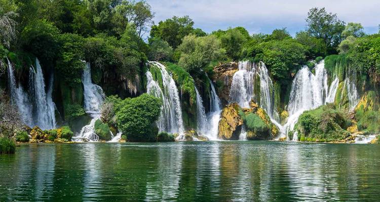 Eine Reihe üppiger grüner Wasserfälle, die in einen klaren smaragdgrünen Pool stürzen, umgeben von dichter Vegetation.