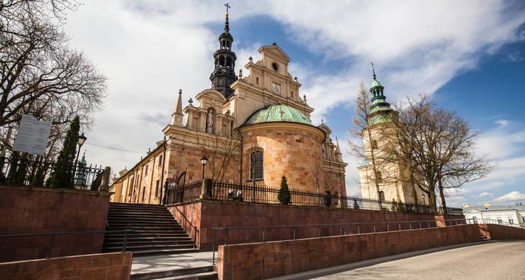 Complexe d'église en pierre avec toit de cuivre à dôme et haute flèche encadré par des arbres nus sous un ciel de printemps.