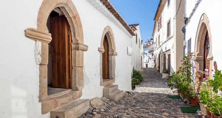 Malerische weiß getünchte Gasse mit gewölbten Fenstern und Kopfsteinpflasterstraße im Alentejo-Sonnenschein.