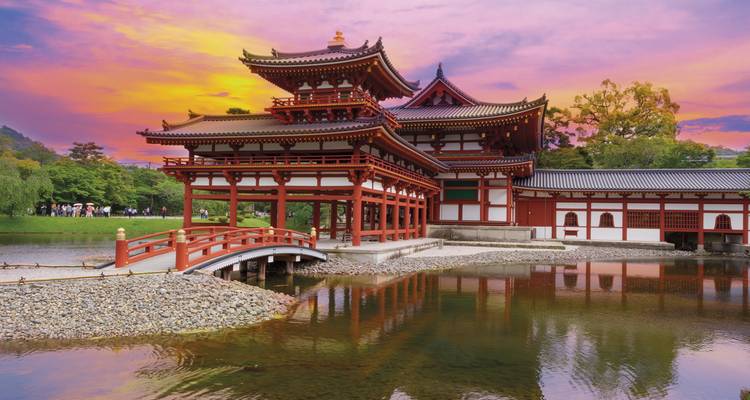 Élégant Pavillon du Phénix Byodo-in vermillon et pont arqué se reflétant dans un étang tranquille sous un ciel de coucher de soleil coloré.