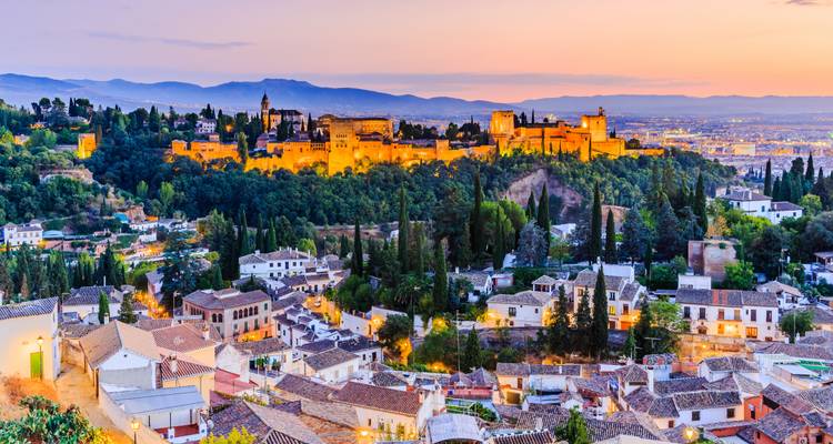 Vue imprenable du coucher de soleil sur une forteresse historique et les lumières de la ville.