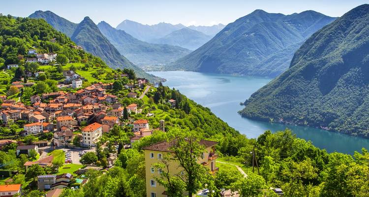 Un village alpin s'étend le long d'une colline verdoyante jusqu'à un vaste lac entouré de montagnes escarpées.