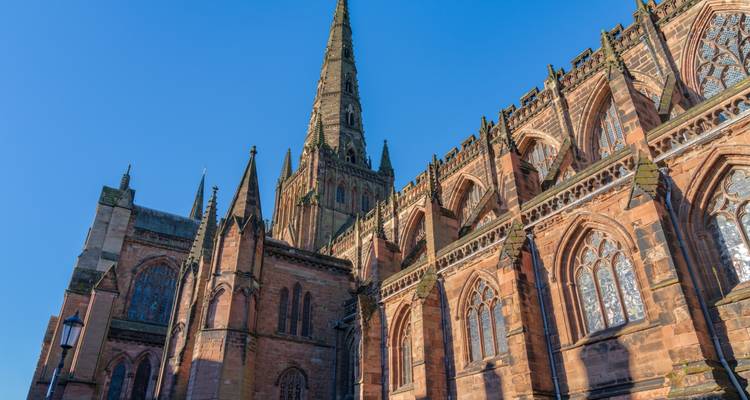 Detailansicht einer großen mittelalterlichen Kathedrale mit hoch aufragender Turmspitze vor klarem blauen Himmel.