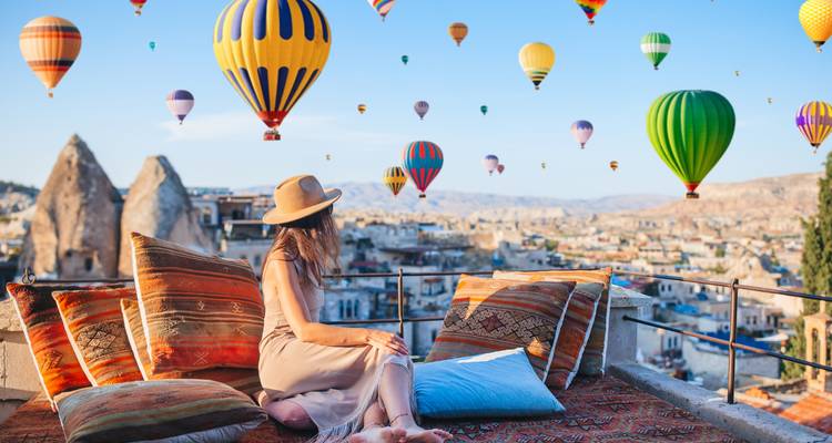 Femme assise sur une terrasse regardant des montgolfières au-dessus de la Cappadoce.