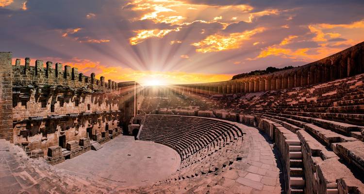 Explosión de rayos solares sobre el teatro romano bien conservado de Aspendos creando rayos de luz dramáticos.