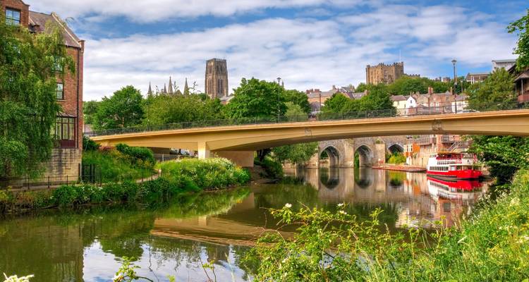 River view of Durham Cathedral and castle with stone arches and greenery on a sunny day.
