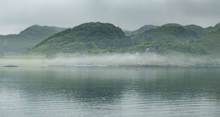 Misty Highland loch with rolling green hills and low cloud.