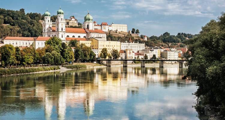 Das historische Passau mit seiner Kathedrale mit zwei Türmen und den farbenfrohen Gebäuden am Flussufer, die sich in der Donau spiegeln.
