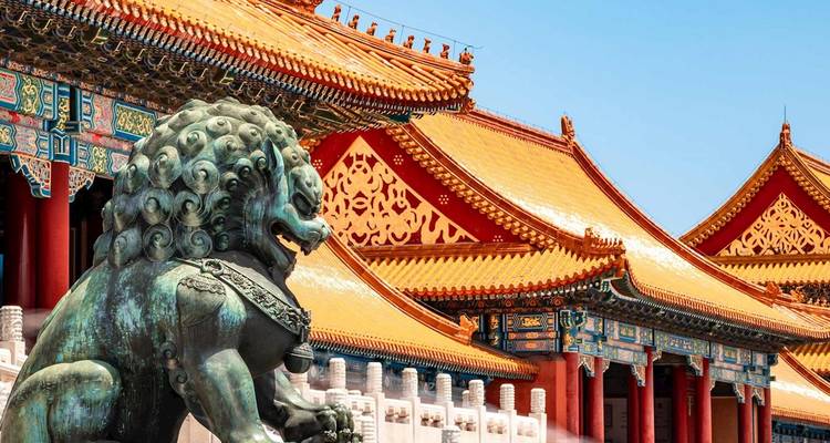 Un león guardián de bronce se alza ante los ornamentados techos dorados de la Ciudad Prohibida de Pekín bajo un cielo azul despejado