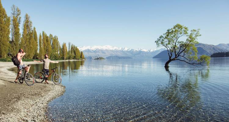 Deux personnes avec des vélos au bord d'un lac avec des montagnes en arrière-plan.