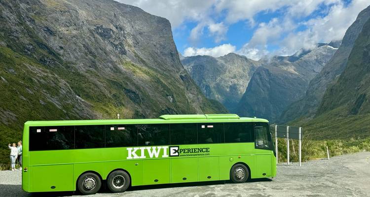 Autobus de tourisme vert garé dans une vallée entourée de montagnes.