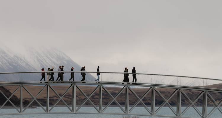 Des gens traversant un pont en arc avec des montagnes enneigées.
