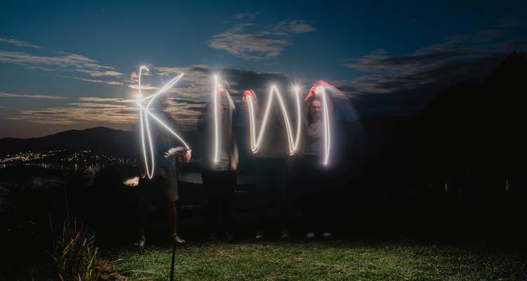 Peinture de lumière créant le mot 'KIWI' la nuit.