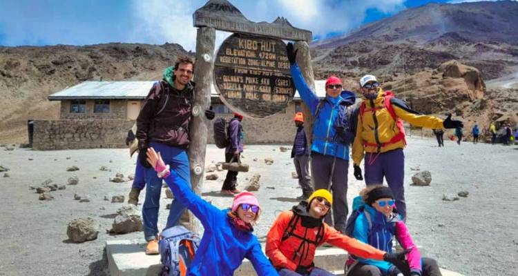 Groupe de randonneurs posant devant le panneau d'un refuge de montagne.
