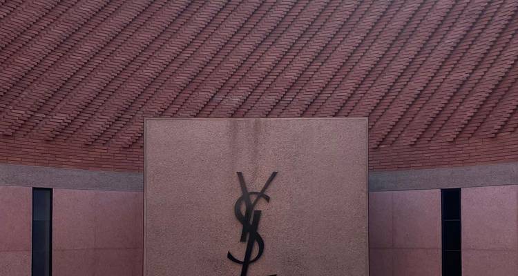 Close-up van de gevel van het Yves Saint Laurent Museum met groot YSL-logo tegen gemusterde bakstenen muur.