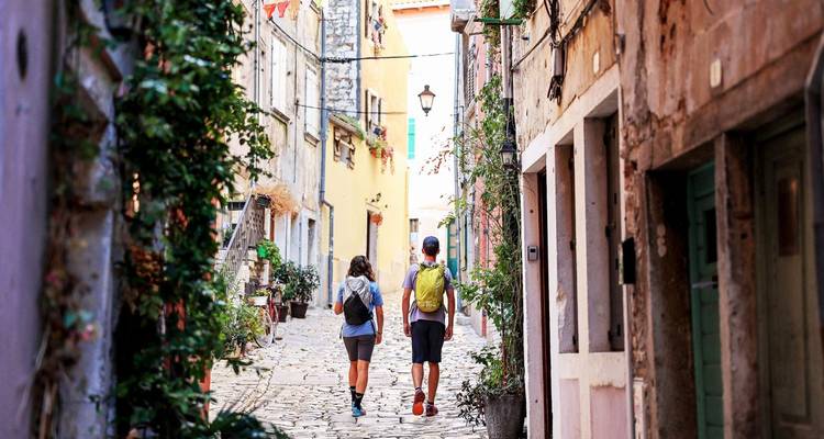 Deux personnes marchant dans une rue étroite pavée de galets.
