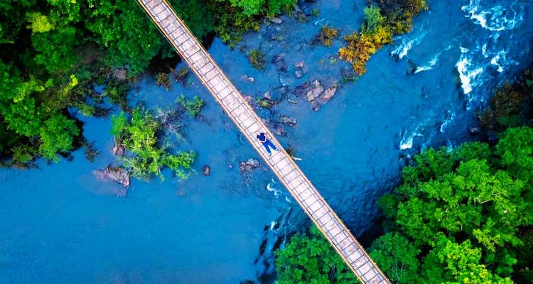 Vue de drone d'un pont suspendu au-dessus d'une rivière avec une végétation luxuriante.