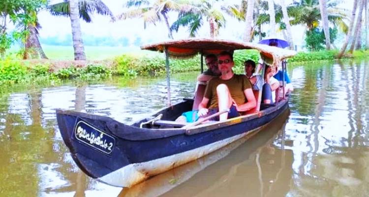 Quelques personnes dans un petit bateau ramant sur une rivière calme entourée de palmiers.