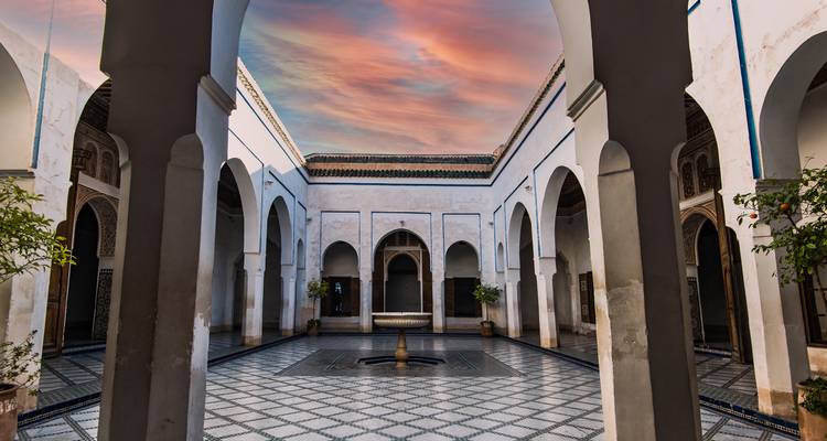 Dekorativer Innenhof mit Bögen und einem Brunnen unter einem Sonnenuntergangshimmel.