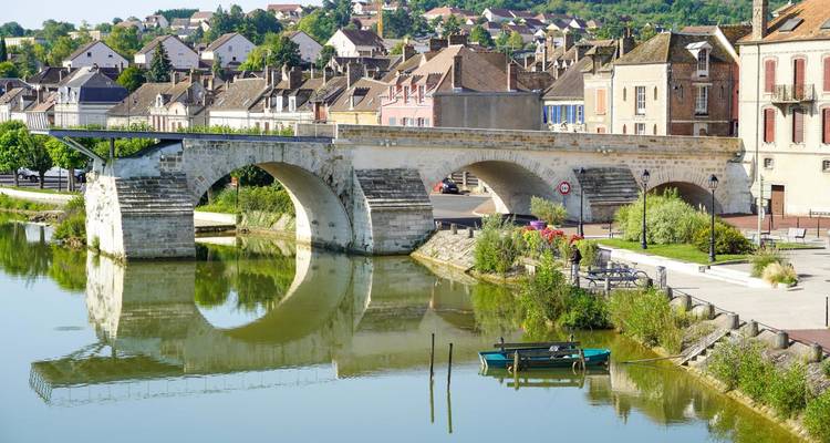 Pont historique au-dessus d'une rivière calme avec une ville en arrière-plan.