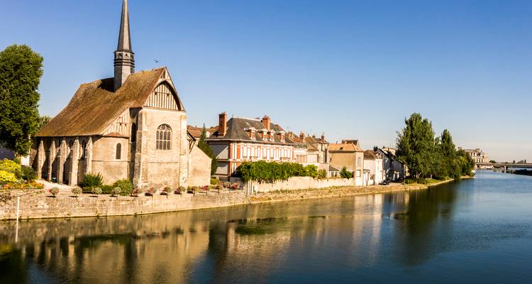 Église gothique au bord d'une rivière, se reflétant dans l'eau.