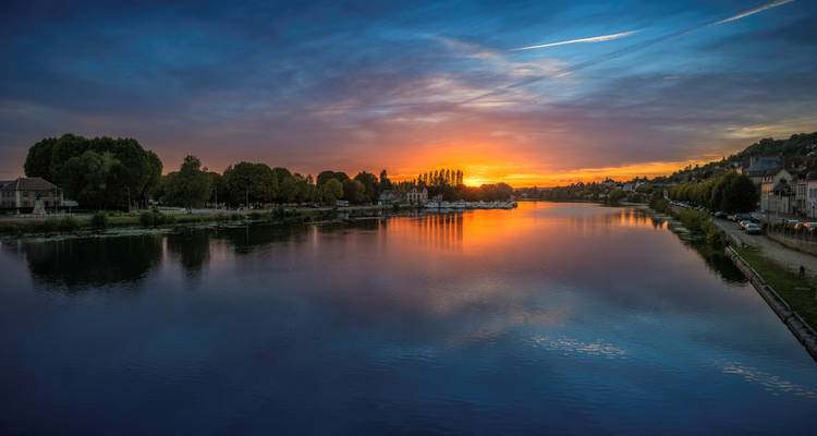 Coucher de soleil sur une rivière calme avec des reflets du ciel.