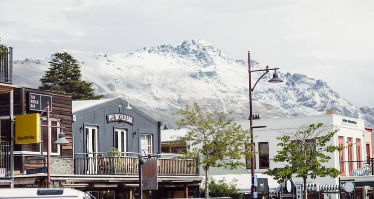 Une rue animée à Queenstown avec des montagnes enneigées en arrière-plan.