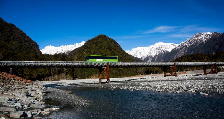 Autobus vert traversant un pont dans un paysage montagneux pittoresque.