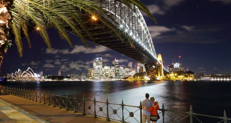 Nachtansicht der Sydney Harbour Bridge mit einem Paar, das über das Wasser blickt.
