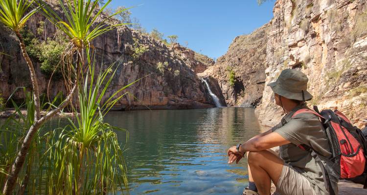 Personne assise près d'une cascade dans un paysage rocheux.
