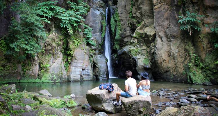 Un couple assis sur un rocher près d'une cascade dans une zone boisée.