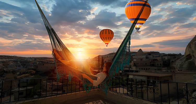 Personne se détendant dans un hamac avec des montgolfières dans le ciel au coucher du soleil.