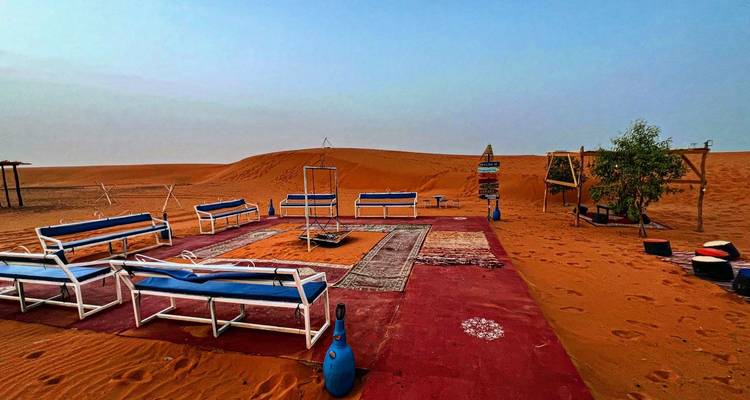 Disposition de sièges extérieurs dans un camp du désert avec des tapis colorés.