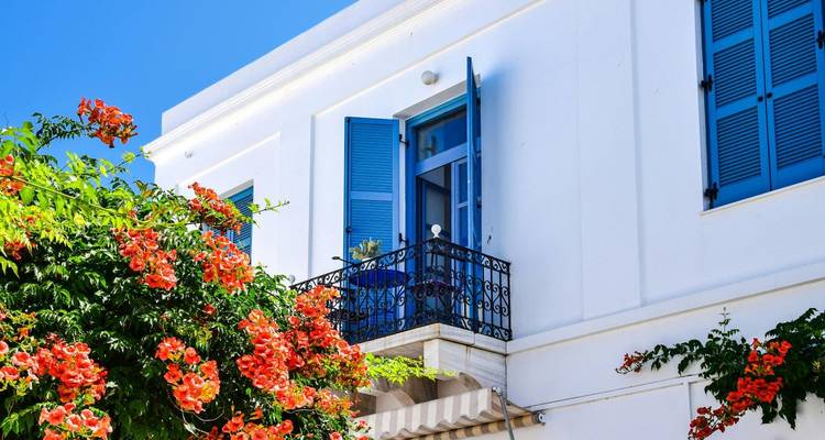 Weißes Gebäude mit blauen Türen und Fenstern, geschmückt mit leuchtenden orangen Blumen, unter einem klaren blauen Himmel.