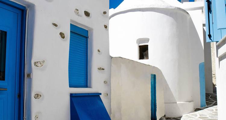 Traditionelle kykladische Architektur mit weißen und blauen Elementen in einer schmalen Straße.
