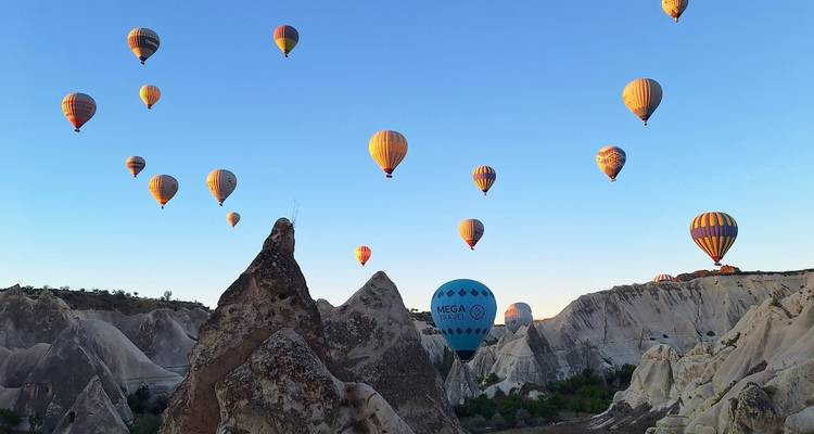 Hot air balloons floating over a rocky landscape during sunrise.