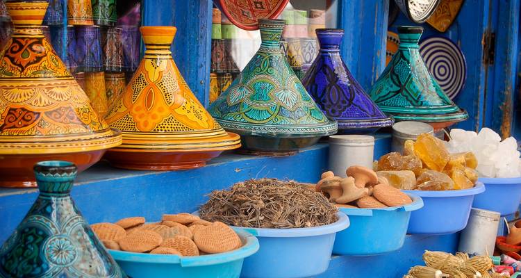 Bunte marokkanische Tajine-Töpfe und verschiedene Gewürze und Süßigkeiten, ordentlich ausgestellt an einem lebendigen Marktstand.