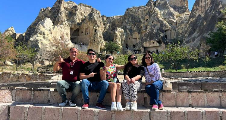 Group of people sitting on steps in front of rocky historical site.