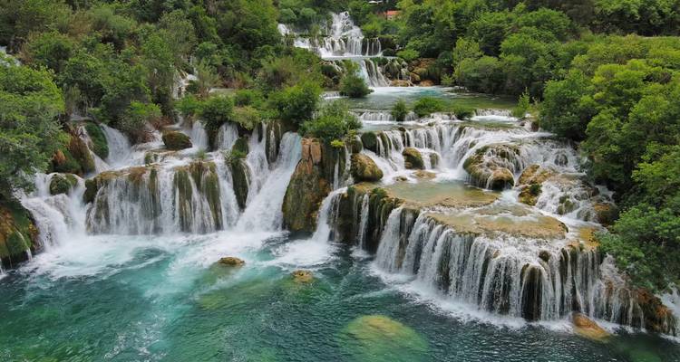 Plusieurs niveaux de chutes d'eau luxuriantes cascadant dans des bassins émeraude entourés d'une forêt dense.