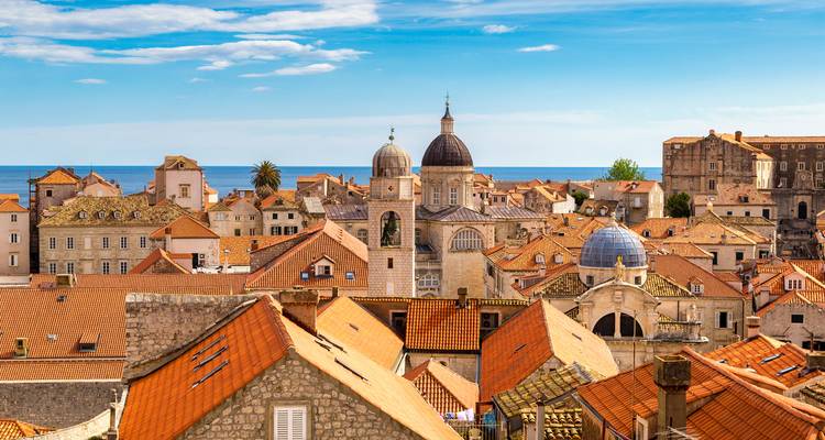 Toits en terre cuite et dômes d'églises de la vieille ville de Dubrovnik sous un ciel bleu éclatant.