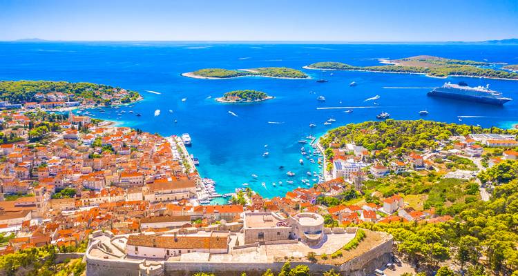 Vue aérienne de la ville de Hvar, de la forteresse et des baies turquoise parsemées d'îles et d'un navire de croisière.