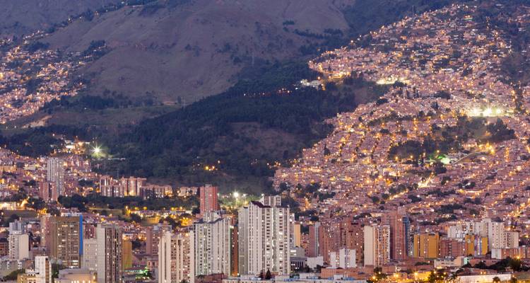 Paysage urbain au crépuscule avec des bâtiments illuminés et un arrière-plan vallonné.