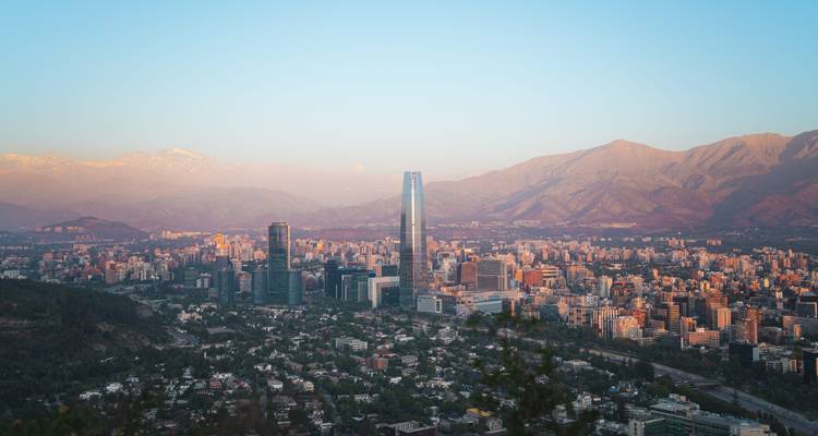 Paisaje urbano al atardecer con edificios modernos altos y montañas.