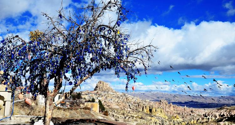 Arbre décoré d'amulettes bleues de mauvais œil sur un paysage rocheux.