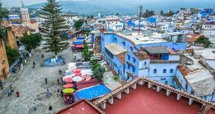 Luftaufnahme von Chefchaouen, Marokko, mit seinen charakteristischen blau getünchten Gebäuden und Hügeln in der Ferne.