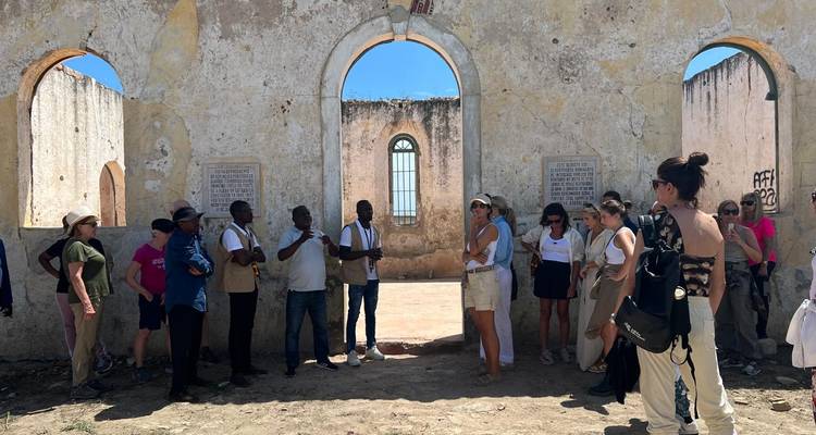 Un groupe de touristes écoute un guide à l'intérieur des ruines ensoleillées d'une ancienne église de pierre aux fenêtres voûtées.