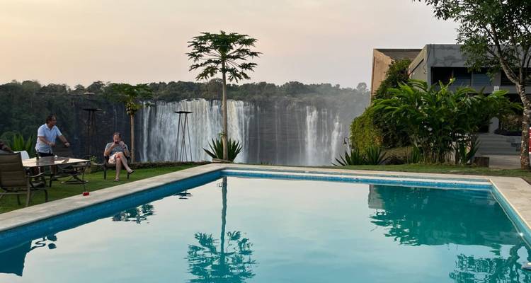Un couple se détend au bord d'une piscine surplombant une cascade spectaculaire et une forêt verdoyante au crépuscule.